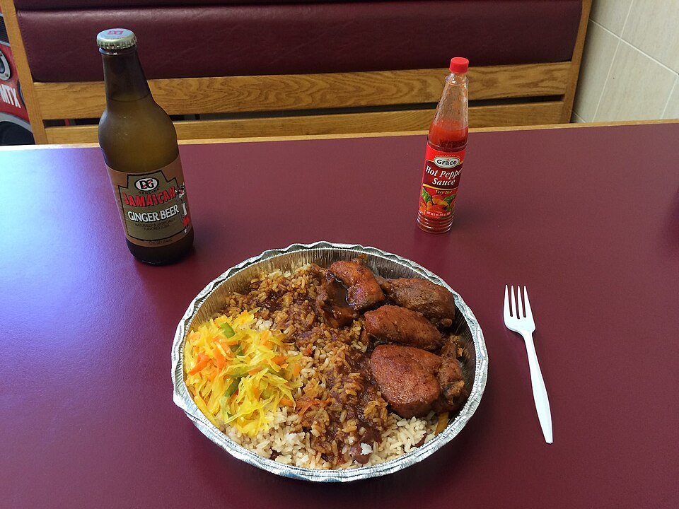 Representative photograph of Brown Stew Chicken. The photograph includes rice and fried plantain as side dishes.