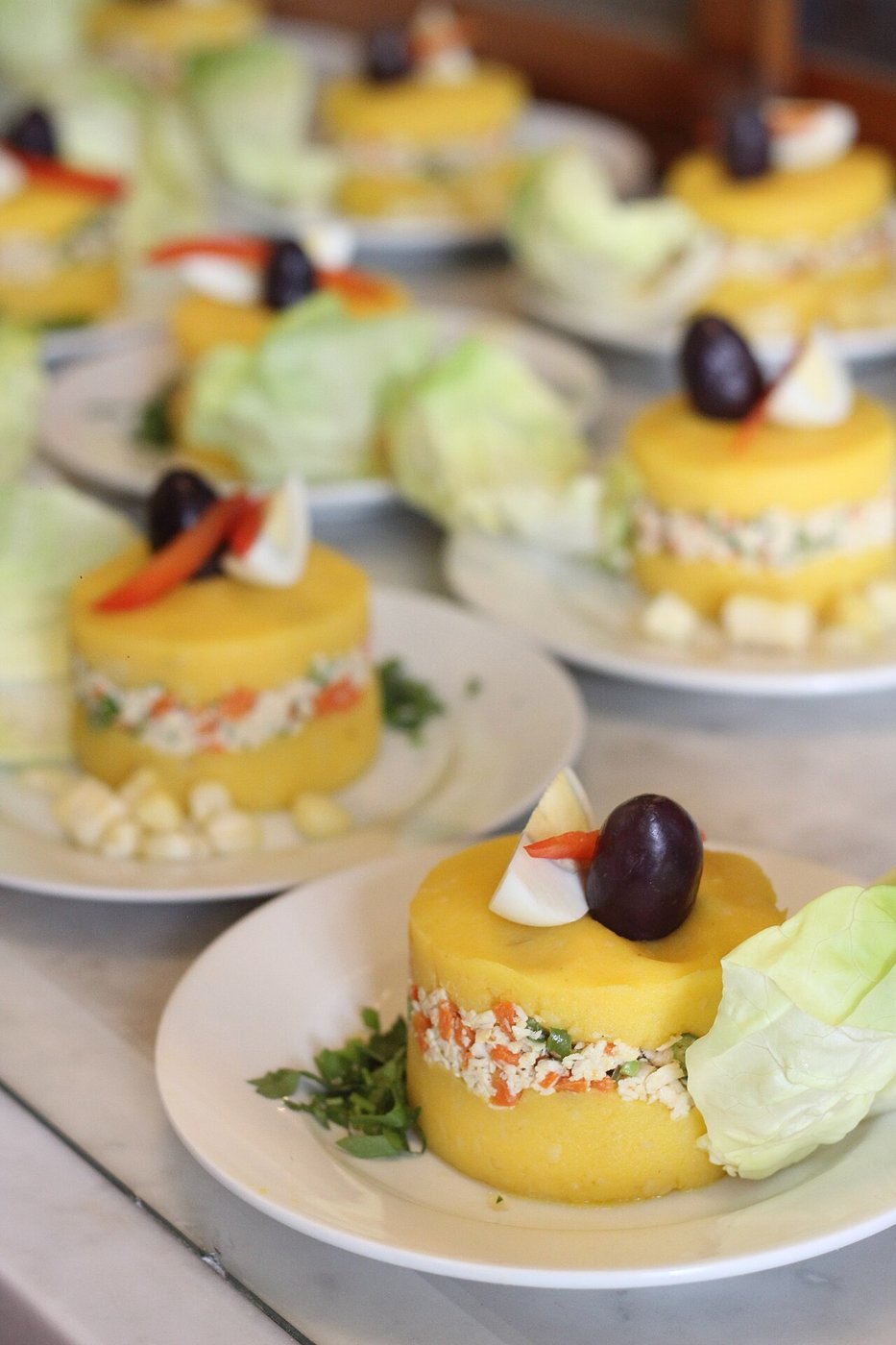 Representative photograph of Causa Limena. The photograph shows individual portions with olives and extra garnish; this draft sets causa in one dish.