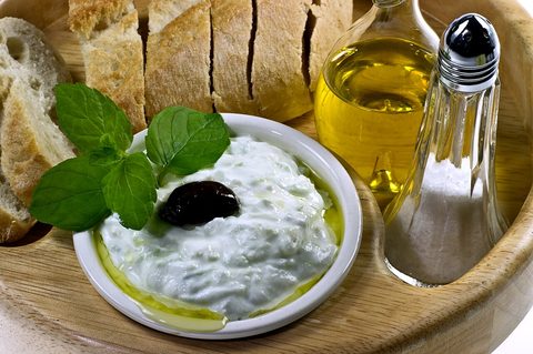 Photograph of cucumber yogurt dip with mint and a black olive, served beside bread