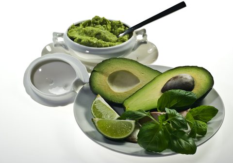 Green guacamole with avocado, lime and basil in front