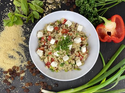 Photograph of couscous salad with feta, red pepper, herbs and raisins in a white bowl