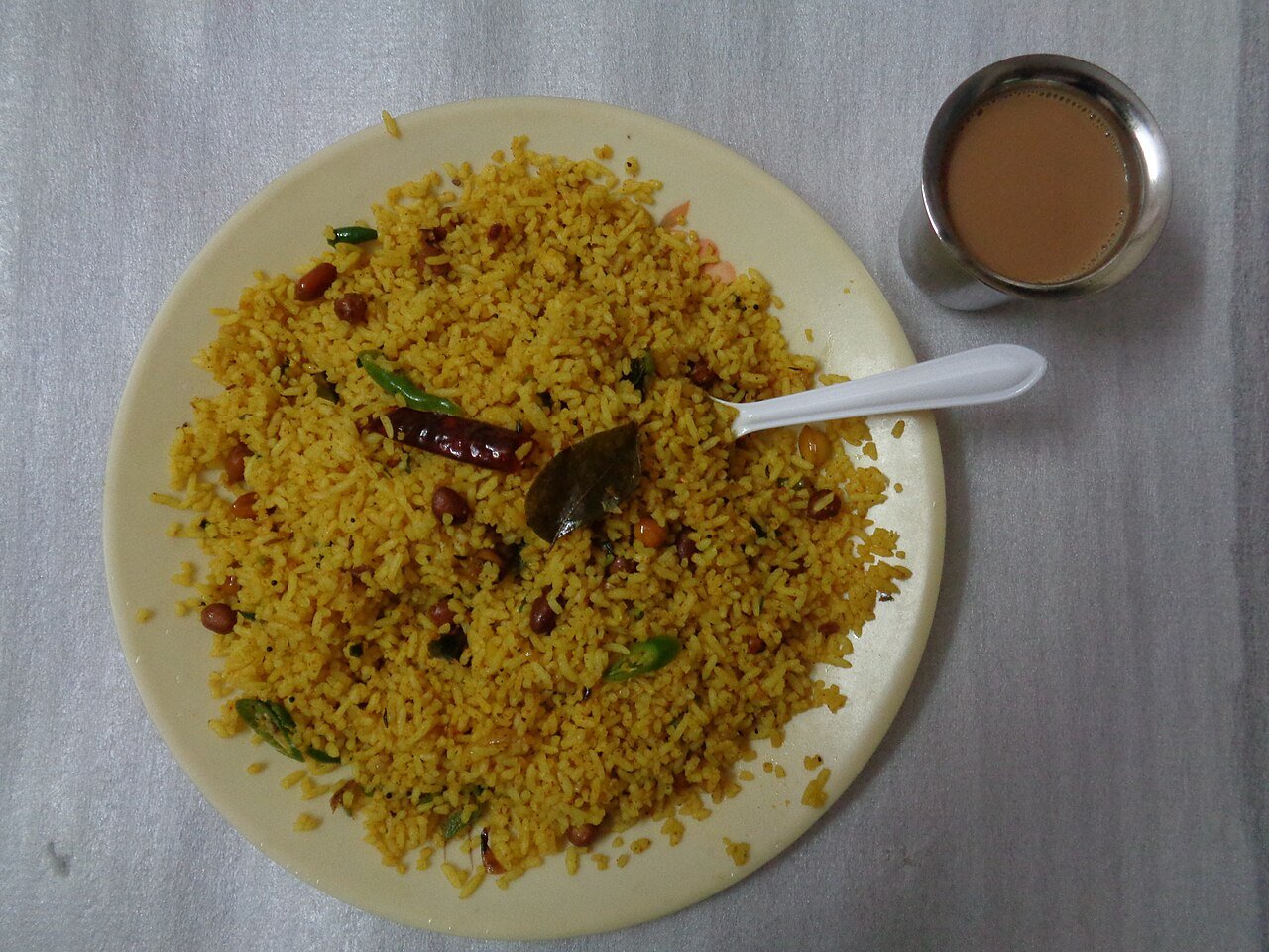 Yellow lemon rice with peanuts and chilies, beside a cup of tea