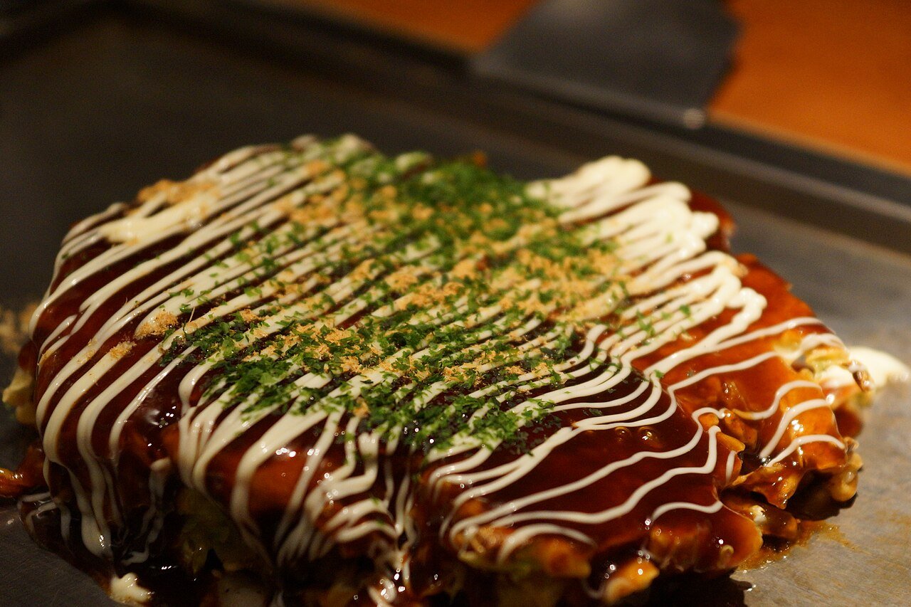 Representative photograph of Okonomiyaki. The photograph includes extra green garnish not included in the draft.