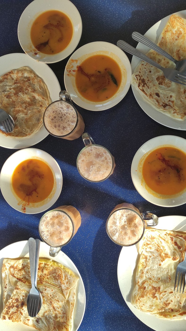 Representative photograph of Roti Canai. The photograph shows a breakfast spread with curry and drinks; this draft makes the roti only.