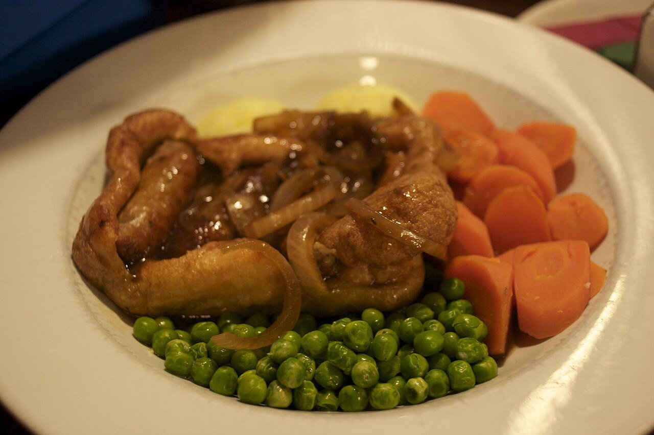 Representative photograph of Toad in the Hole. The photograph includes gravy, peas and carrots not included in this draft.